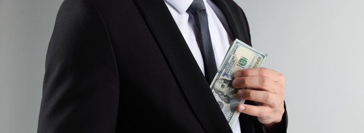 Photo of Man putting dollars in pocket on light background, closeup