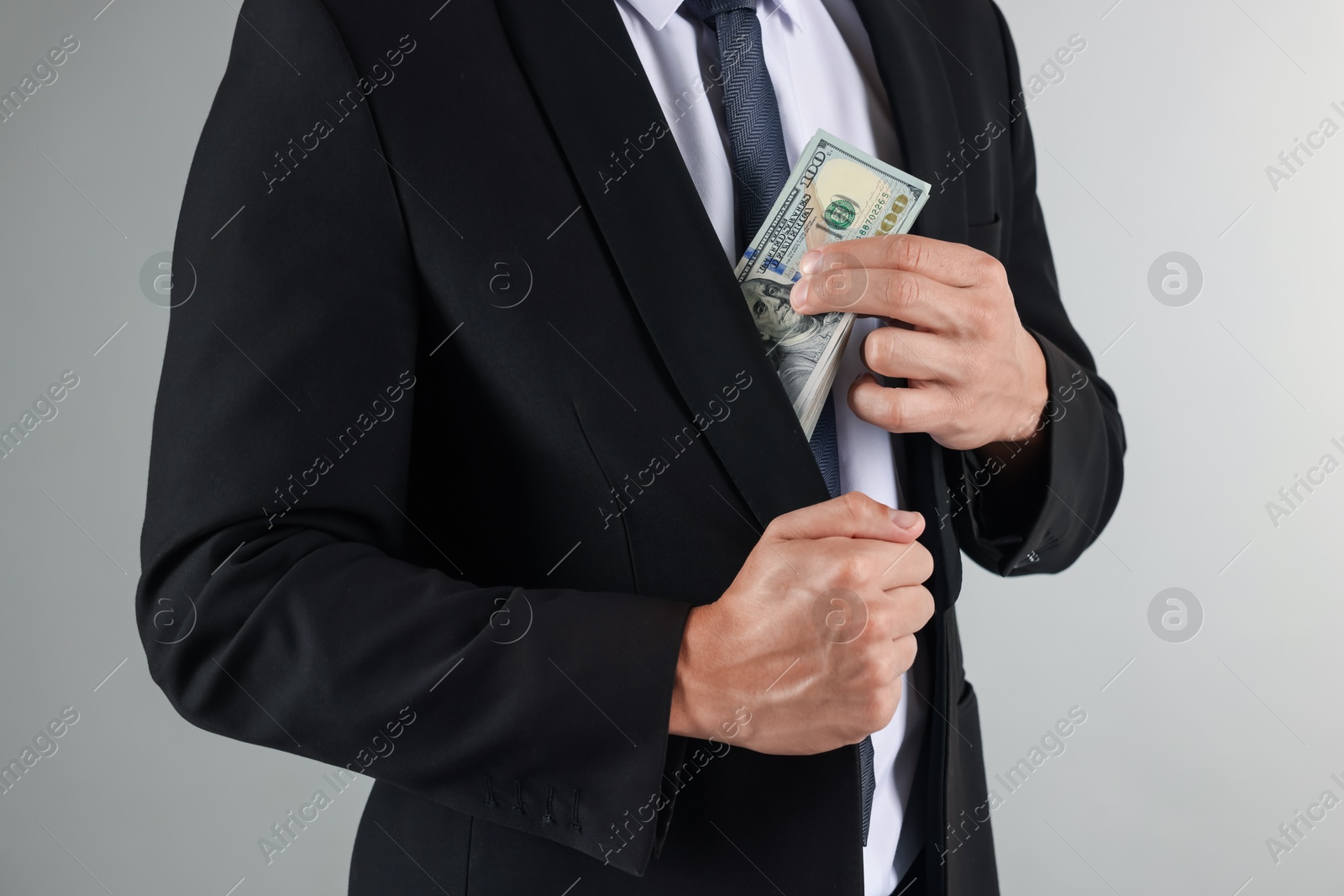 Man putting dollars in pocket on light background, closeup Photo of Man putting dollars in pocket on light background, closeup