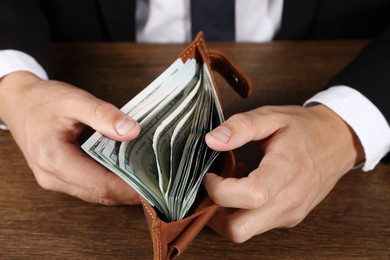 Photo of Man with dollars in wallet at wooden desk, closeup