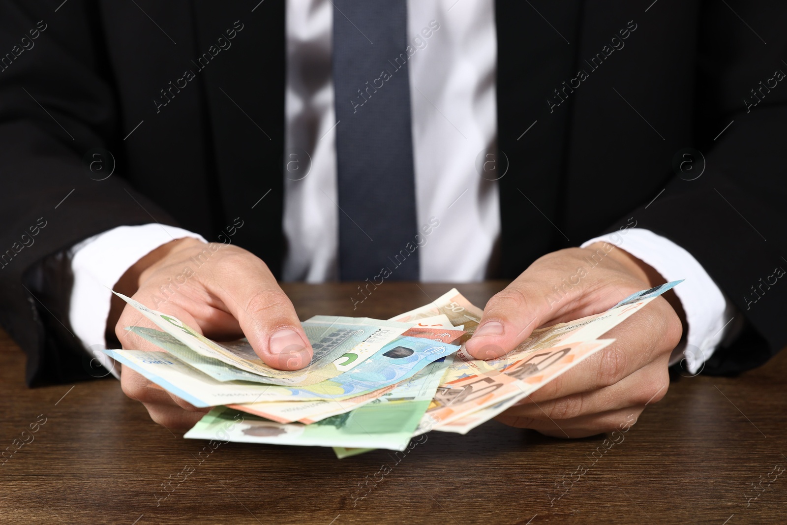 Photo of Man with euro banknotes at wooden desk, closeup
