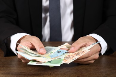 Photo of Man with euro banknotes at wooden desk, closeup