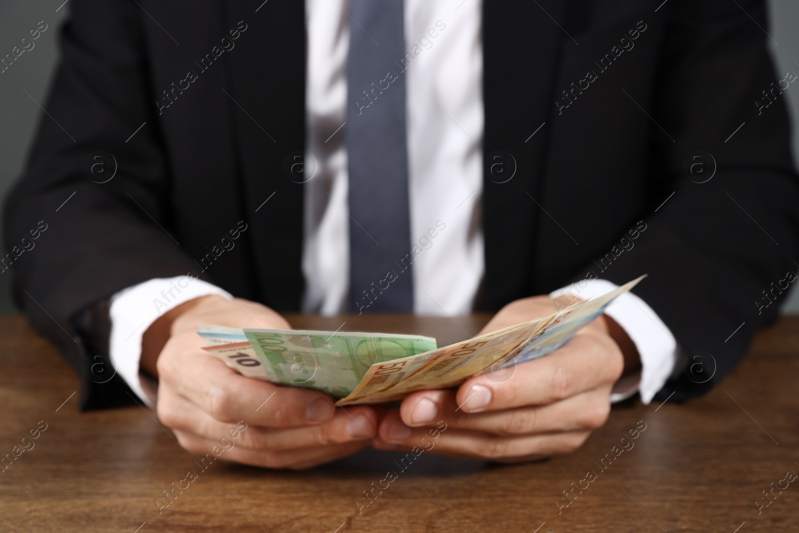 Man with euro banknotes at wooden desk, closeup Photo of Man with euro banknotes at wooden desk, closeup