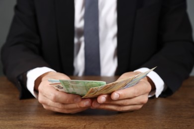 Photo of Man with euro banknotes at wooden desk, closeup