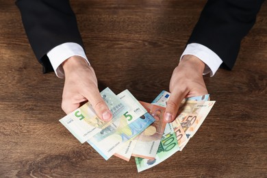 Photo of Man with euro banknotes at wooden desk, above view