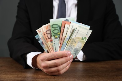 Photo of Man with euro banknotes at wooden desk, closeup