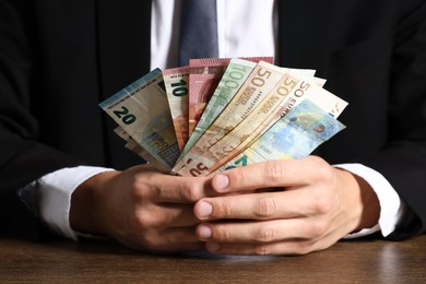 Photo of Man with euro banknotes at wooden desk, closeup