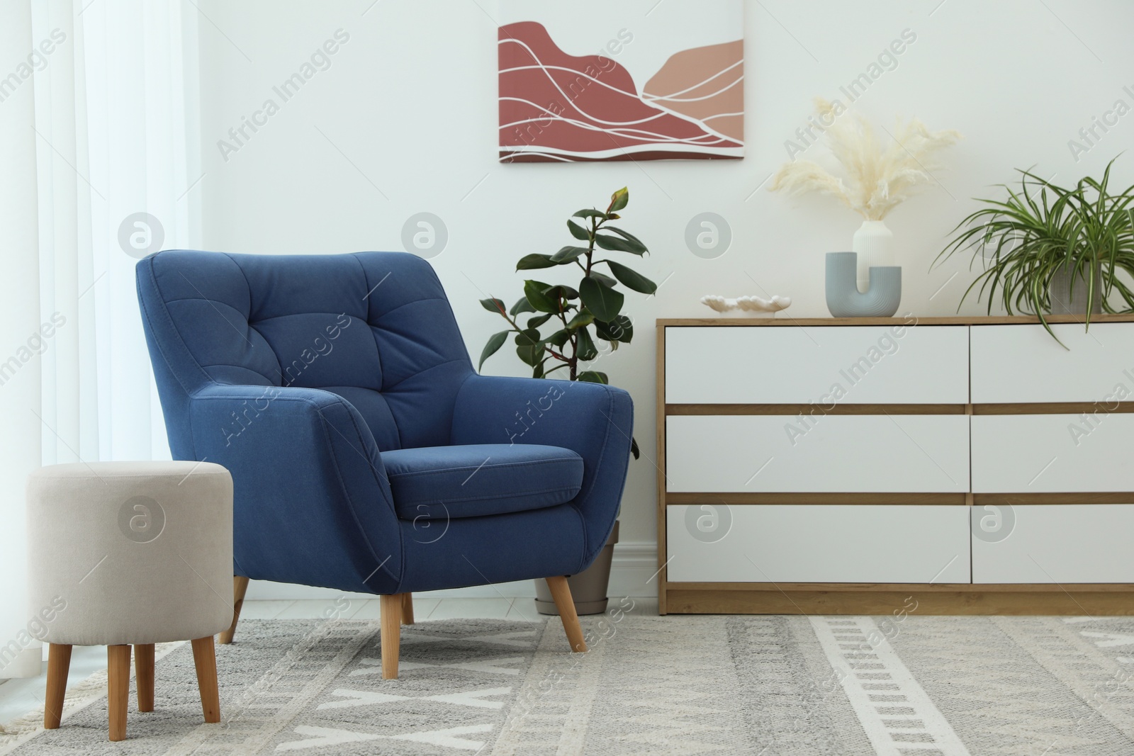 Photo of Stylish blue armchair, chest of drawers, pouf and houseplants indoors. Interior design