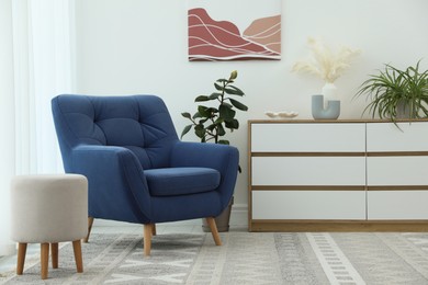 Photo of Stylish blue armchair, chest of drawers, pouf and houseplants indoors. Interior design