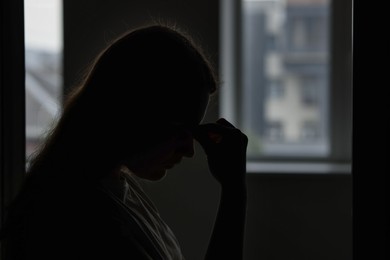 Photo of Silhouette of sad young woman at home, space for text