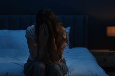 Photo of Sad young woman sitting on bed at home, space for text