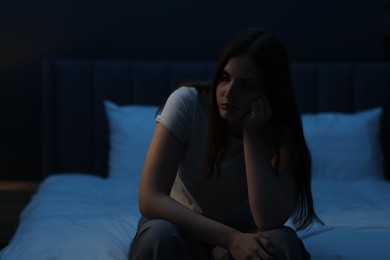 Photo of Sad young woman sitting on bed at home