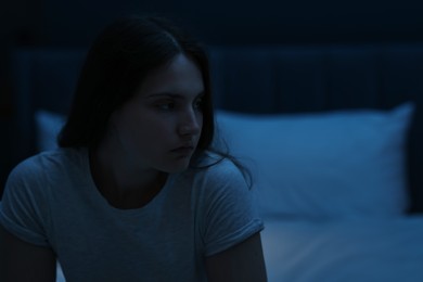 Photo of Sad young woman sitting on bed at home, space for text