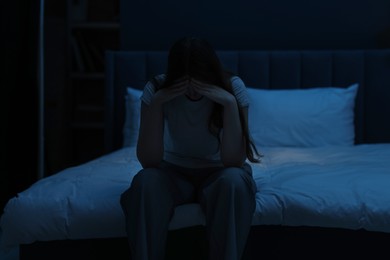 Photo of Sad young woman sitting on bed at home