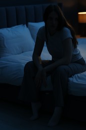 Photo of Sad young woman sitting on bed at home