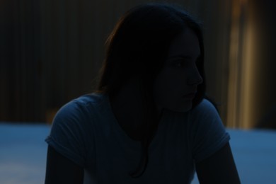 Photo of Sad young woman sitting on bed at home