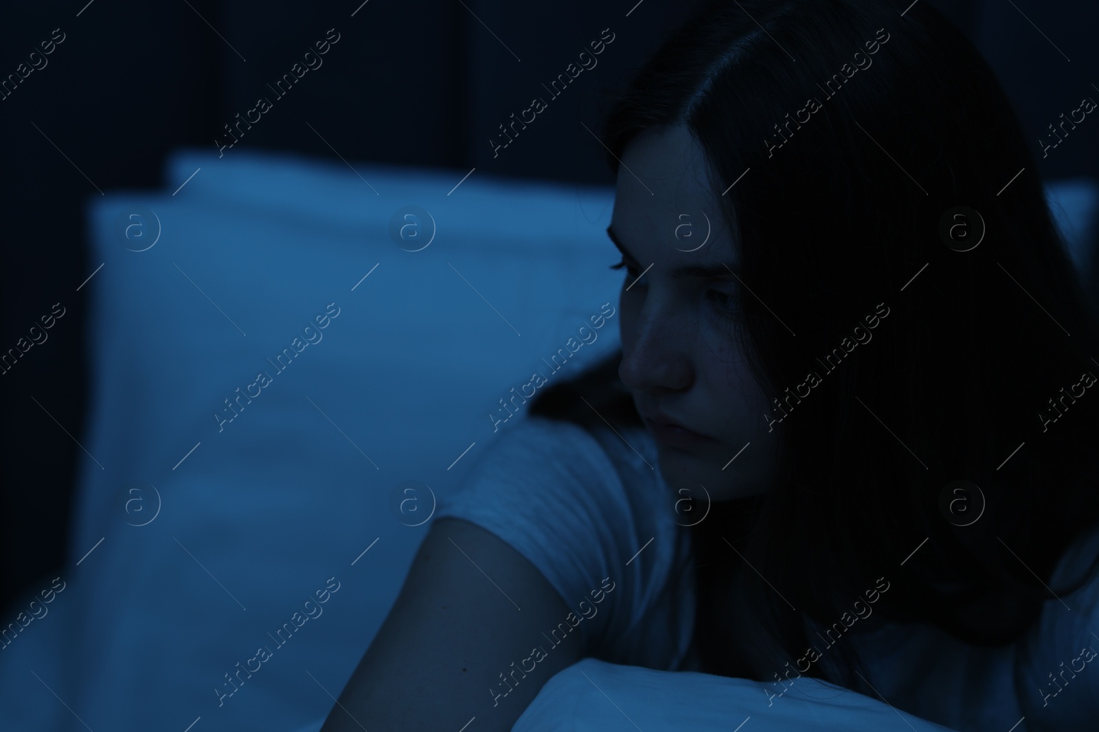 Sad young woman sitting on bed at home, space for text Photo of Sad young woman sitting on bed at home, space for text