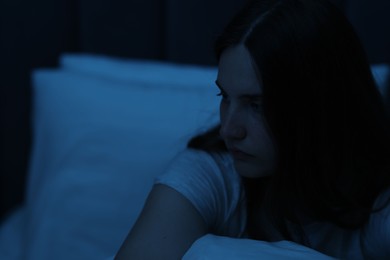 Photo of Sad young woman sitting on bed at home, space for text