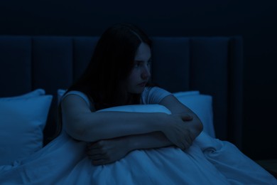 Photo of Sad young woman sitting on bed at home