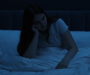 Photo of Sad young woman sitting on bed at home