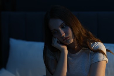 Photo of Sad young woman sitting on bed at home, space for text