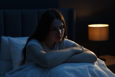 Photo of Sad young woman sitting on bed at home