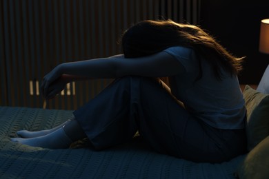 Photo of Sad young woman sitting on bed at home