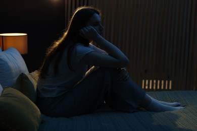 Photo of Sad young woman sitting on bed at home