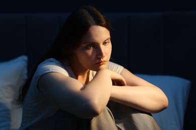 Photo of Sad young woman sitting on bed at home