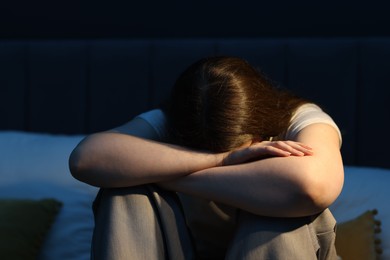 Photo of Sad young woman sitting on bed at home