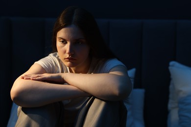 Photo of Sad young woman sitting on bed at home