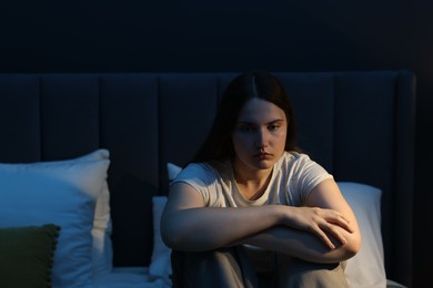 Photo of Sad young woman sitting on bed at home
