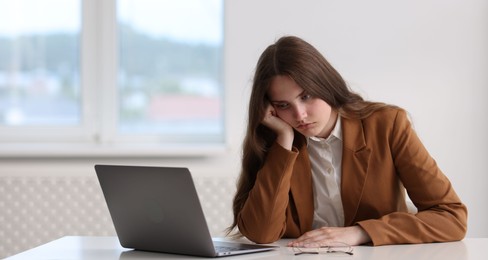 Photo of Sad young woman with laptop at white table in office