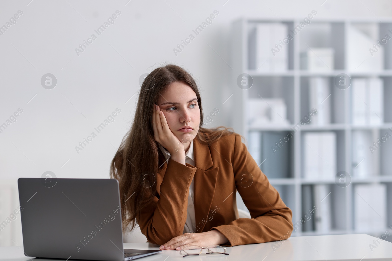 Sad young woman with laptop at white table in office Photo of Sad young woman with laptop at white table in office