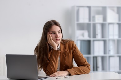 Photo of Sad young woman with laptop at white table in office
