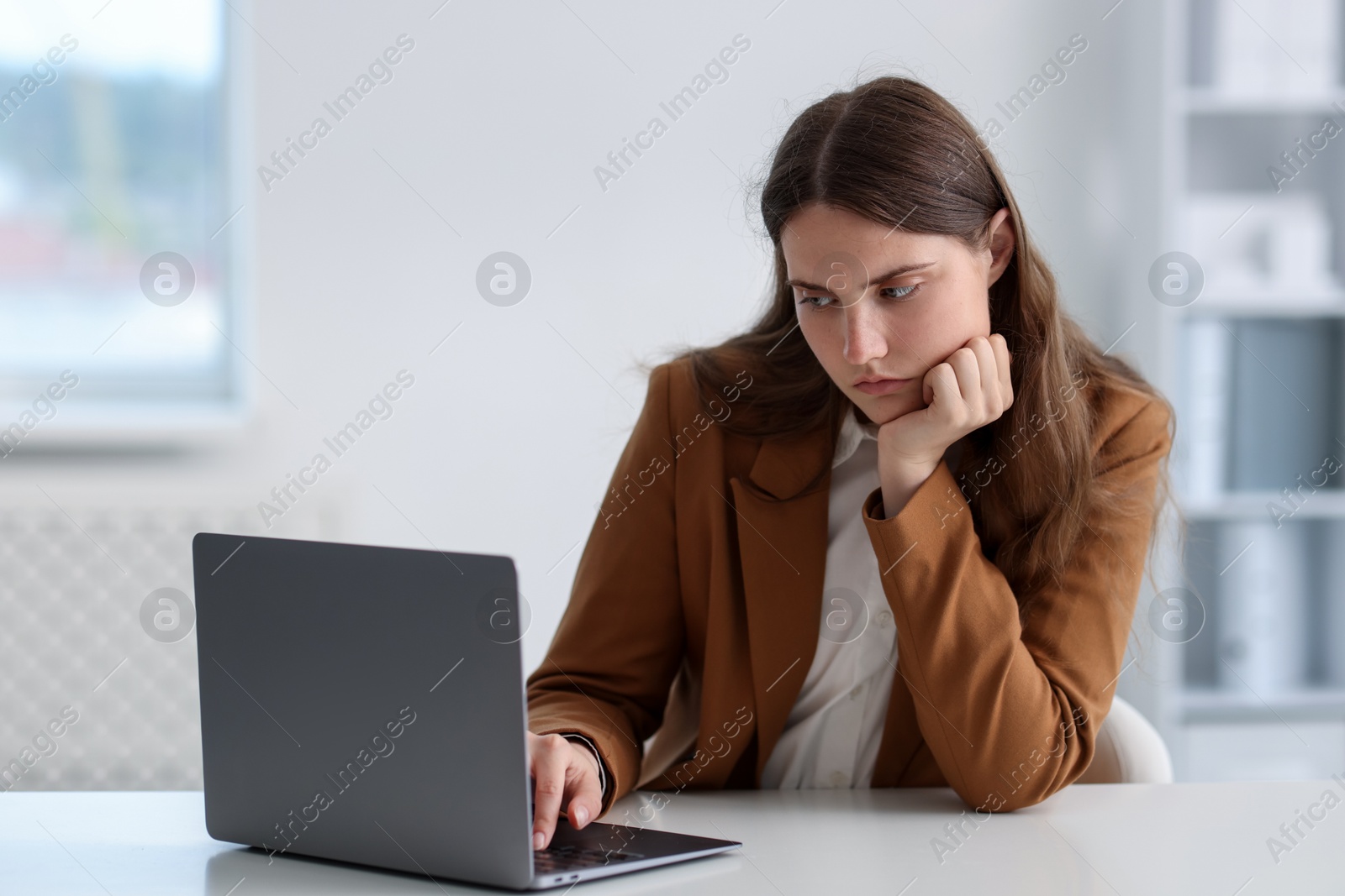 Sad young woman with laptop at white table in office Photo of Sad young woman with laptop at white table in office