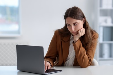 Photo of Sad young woman with laptop at white table in office