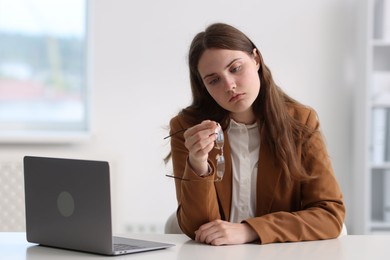Photo of Sad young woman with laptop at white table in office