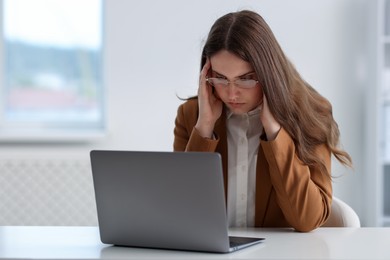 Photo of Sad young woman with laptop at white table in office