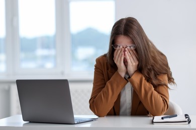 Photo of Sad young woman with laptop at white table in office