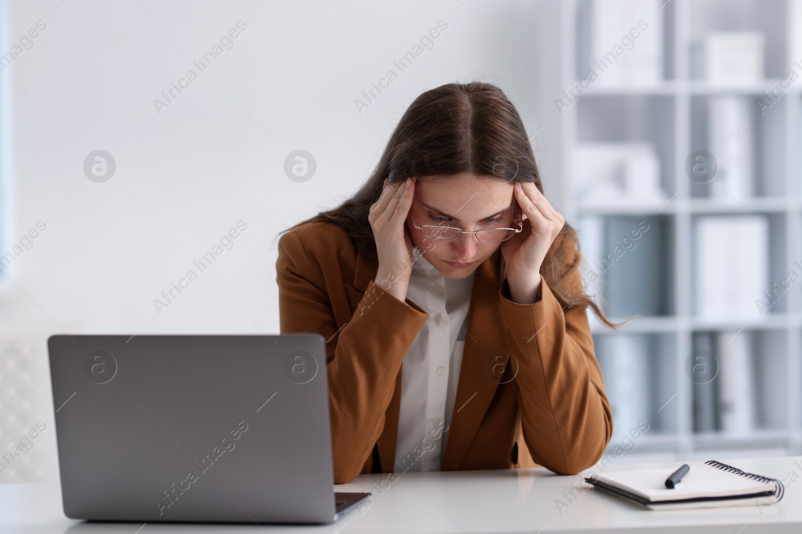 Sad young woman with laptop at white table in office Photo of Sad young woman with laptop at white table in office