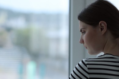 Photo of Sad young woman near window at home, space for text