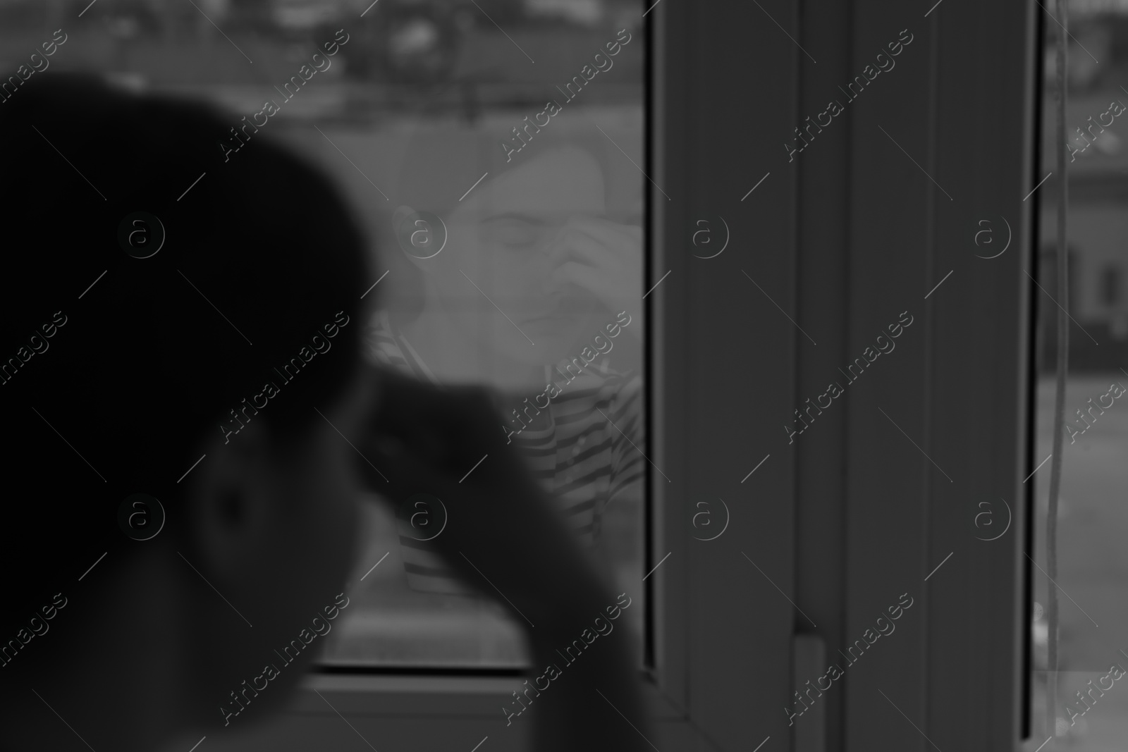 Sad young woman near window at home, selective focus and space for text. Black and white effect Photo of Sad young woman near window at home, selective focus and space for text. Black and white effect