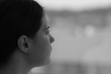Photo of Sad young woman near window at home, closeup and space for text. Black and white effect