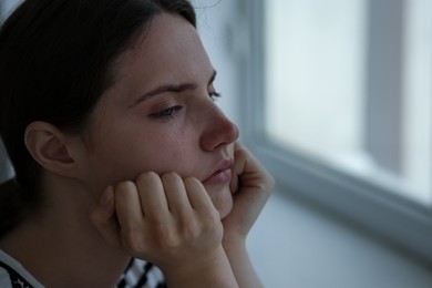 Photo of Sad young woman near window at home, closeup. Space for text