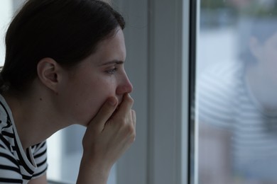 Photo of Sad young woman near window at home, space for text