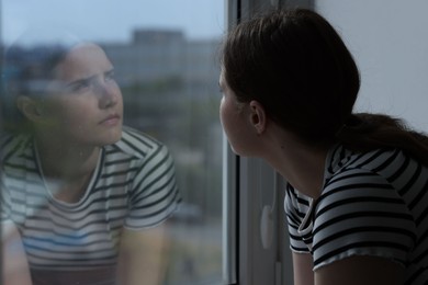 Photo of Sad young woman near window at home, space for text
