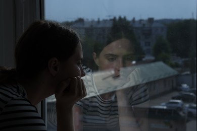 Photo of Sad young woman near window at home, space for text