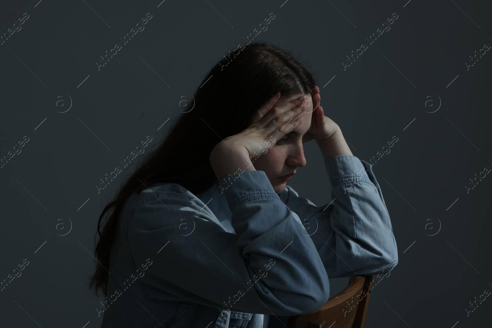 Sad young woman sitting on chair near grey wall indoors Photo of Sad young woman sitting on chair near grey wall indoors