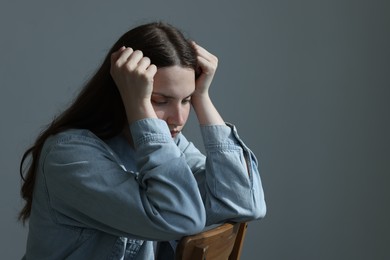 Photo of Sad young woman sitting on chair near grey wall indoors, space for text