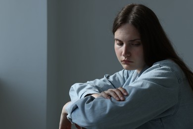 Photo of Sad young woman near grey wall indoors, space for text